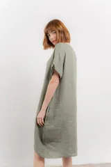 Vestido corto color verde oliva, confeccionado en lino, con corte recto y mangas cortas. Presenta bolsillos laterales y botones decorativos en los laterales.