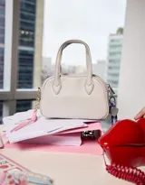 Cartera bowling color gris claro de cuerina con doble asa corta de mano, correa regulable y cierre superior.