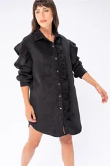 Camisa larga negra de poliéster con textura de pana fina, con mangas largas y cierre frontal con botones. Presenta volados verticales en el frente.
