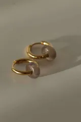 Par de aros tipo argolla dorados con dije de piedra natural con patrón de manchas negras sobre fondo blanco.