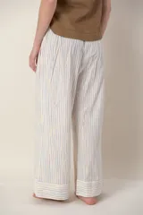 Pantalón ancho de lino color crudo con rayas verticales en tonos celeste, naranja y rosa. Tiene bolsillos laterales y cierre con botones a la vista en el lateral.