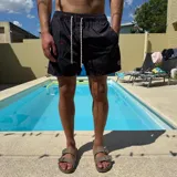 Short de baño negro con estampado de siluetas rojas, cintura elástica con cordón blanco y logo de la marca en la pierna.