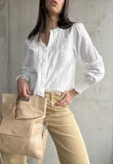 Camisa blanca de manga larga con detalles de broderie y calados en el frente y las mangas. Tiene cuello mao y cierre frontal con botones. Los puños son elásticos.