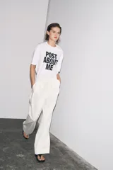 Camiseta blanca de corte amplio, cuello redondo y mangas cortas. Estampado frontal con la frase "Post About Me" en letras negras.