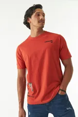 Remera de manga corta color ladrillo, con cuello redondo y estampado con texto y diseño abstracto en el frente.