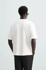 Camiseta verde oscuro de corte holgado, confeccionada en tejido de algodón grueso. Tiene cuello redondo y mangas cortas sin costura en la sisa.