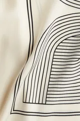 Pantalón de corte recto color crema con estampado geométrico en negro. Modelo de tiro alto con elástico en la parte posterior de la pretina y cierre oculto en un lateral.
