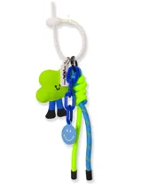 Llavero con un dije de peluche verde con forma de nube y piernas azules, un dije redondo azul con una cara sonriente, una cadena de eslabones azules y cordones trenzados de color azul y verde neón.
