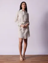 Vestido camisero corto a rayas verticales color beige, con cuello con solapa, abertura central con botones, bolsillos aplicados en el pecho y lazo de ajuste en la cintura.
