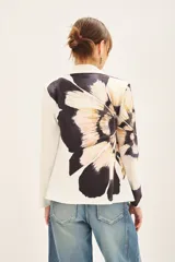 Blazer con estampado abstracto en tonos beige, negro y blanco. Tiene solapas blancas y está adornado con tachas termofijadas en el frente. Se cierra con un cinturón negro con una flor grande.