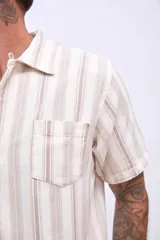 Camisa de manga corta color beige con rayas verticales marrones, cuello tipo cubano y bolsillo en el pecho.