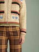 Cardigan de punto color beige con cierre frontal, cuello tortuga y mangas largas holgadas. Presenta diseño con distintas texturas, tejido en ochos a los lados del cierre y apliques de corazones de tela bordados. Confeccionado en 100% algodón.