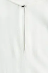 Blusa color blanco hueso de tejido de crepé de viscosa con cuello redondo y abertura de cerradura con botón de metal pequeño adelante. Mangas japonesas de corte raglán y bajo levemente redondeado.