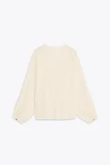 Blusa color crema de tejido arrugado con hilo metalizado, cuello redondo con escote en pico, manga larga abullonada y nudo delantero. Cierre frontal con botones con flores bordadas.