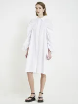 Vestido camisero blanco con botones frontales, cuello camisero, manga larga abullonada con puños ajustables y corte a la rodilla.