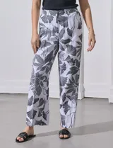 Pantalón de lino blanco con estampado de hojas en negro, de corte recto y pretina ancha con pasadores. Tiene bolsillos delanteros y bolsillos ojal simulados en la parte trasera.