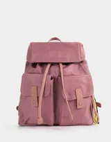 Mochila de tela color lila, con solapa con broche y tira de ajuste, doble bolsillo frontal con broche y pouch con charm lateral en forma de cartera.