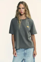 Camiseta gris de algodón con efecto lavado, cuello redondo, manga corta y parches estampados en el frente.