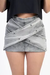 Minifalda gris de jean con diseño cruzado y tachas plateadas.