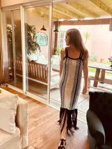 Vestido largo tejido en lurex color beige con diseño vertical y terminación en flecos negros. Breteles finos de cuero intervenido a mano con tientos de cuero plateado.