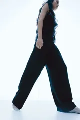 Pantalón sastrero negro de sarga con pinzas, corte holgado, tiro alto, pretina prolongada con botón, bolsillos al bies y bolsillos insertados atrás. Piernas anchas con pliegues adelante y atrás.