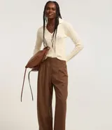 Pantalón de vestir marrón con finas rayas verticales blancas, de corte recto y tiro alto. Se ajusta a la cintura con cinturón de cuero marrón.