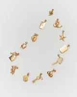 Dije dorado con forma de llave y textura efecto arena, con circonita engarzada.