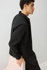 Sobrecamisa negra de corte recto, con cuello clásico, cierre frontal con botones, dos bolsillos de parche con solapa en el pecho, mangas largas con puños abotonados y bajo redondeado.