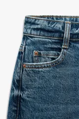 Pantalón de jean gris oscuro, de corte mom fit, tiro alto y largo tobillero. Cuenta con cinco bolsillos, cierre frontal con cremallera y botón.