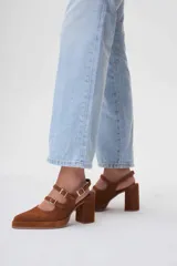 Zapato de cuero marrón con taco bloque, punta fina y dos tiras con hebillas doradas.