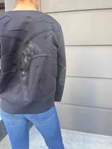 Cardigan negro de tejido fino en lana, con cuello redondo, cierre frontal con botones y detalle de cuero en los puños.