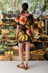 Vestido camisero corto con estampado abstracto en tonos naranja, rosa, amarillo y negro. Tiene cuello camisero, mangas cortas y cierre frontal con botones. Incluye lazo en la cintura para ajustar.