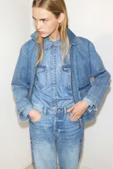 Campera de denim azul de algodón rígido con cuello, cierre delantero y canesú en la espalda. Modelo con puños abotonados, bolsillos delanteros con solapa y bolsillo interior de parche en el pecho. Trabillas ajustables con botones en la parte posterior del bajo.