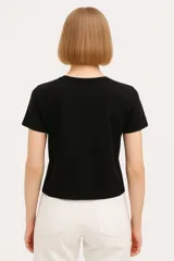 Remera negra de manga corta con estampado frontal que incluye la palabra "Believe" en letras doradas con efecto foil y un diseño abstracto con patrones de cebra y piel de animal.