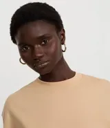 Blusa color beige, cropped y de corte amplio, confeccionada en tejido de media malla, con cuello redondo y mangas cortas.