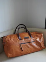 Bolso de viaje tipo weekender de cuero color marrón, con doble asa corta y correa larga desmontable. Cuenta con cierre superior, bolsillos internos y externos con cierre metálico. Forro interior de tela. Marca Sierra Mora.