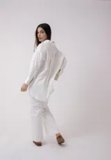 Camisa blanca de lino, de corte holgado, con cuello clásico, cierre frontal con botones, bolsillo en el pecho y mangas largas con puños abotonados.