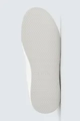 Zapatillas deportivas blancas con detalle de color marrón en el talón y suela con volumen.