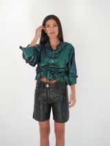 Camisa verde esmeralda con reflejos tornasolados, de corte holgado, con cuello camisero, cierre frontal con botones de nácar y mangas largas con puños abotonados.