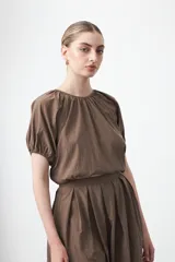 Top negro de manga corta con escote redondo y frunces en la costura de la sisa, creando un efecto de manga abullonada. El tejido parece ligero y con textura.