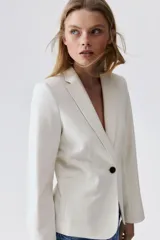 Blazer entallado color blanco, con solapas de muesca y cierre de un botón. Bolsillos de adelante ribeteados, botones decorativos en los puños y abertura atrás.
