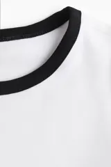 Remera blanca entallada de punto suave con ribete fino negro en cuello y mangas cortas.