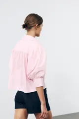 Camisa rosada de popelina de algodón, con cuello clásico, manga corta abullonada y cierre frontal con botones.