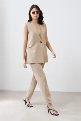 Chaleco largo color beige con solapas, sin mangas y con un botón metálico.