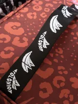 Bolso térmico (cooler bag) de gran tamaño, color marrón rojizo, con estampado mixto de leopardo y cebra. Posee manija superior y correa ajustable para hombro, ambas de cinta blanca con estampado negro de monograma.