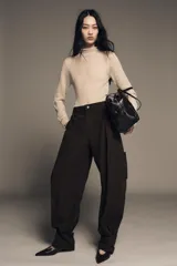 Pantalón cargo de algodón color marrón oscuro, tiro medio, con pliegues frontales, bolsillos delanteros ocultos y bolsillos de plastrón con solapa y botones a presión en las piernas. El bajo del pantalón tiene una trabilla con botón y se muestra doblado hacia afuera.