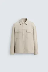 Sobrecamisa color beige de corte relaxed fit, con cuello solapa, manga larga con puños abotonados, bolsillos de plastrón con solapa en el pecho y bolsillos de vivo en la cadera. Cierre frontal con botones.