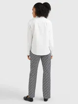 Camisa blanca de algodón orgánico con corte regular, cuello mao con volantes, cierre frontal con botones, mangas largas con puños abotonados y logo bordado en el ruedo.