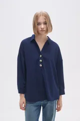 Blusa azul marino de corte holgado, con cuello camisero y mangas largas. Tiene una abertura en V con tres botones en el frente.