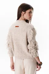 Sweater color beige de tejido de punto con cuello redondo y mangas largas con flecos.